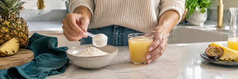 Hand comparing a plain scoop of white powder and a small clear cup of tropical liquid on cream kitchen counter, teal cloth, both options sharply photographed.
